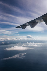 Plane window view with blue sky and beautiful clouds, sky. As seen through window of an aircraft. View of wing, ocean, volcano Agung & Nusa Penida. Airplane from island Bali to Labuan Bajo, Komodo.