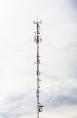 Tall red and white antenna on cloudy sky.