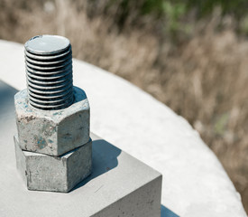 Two nuts threaded on bolt attached to cement block.