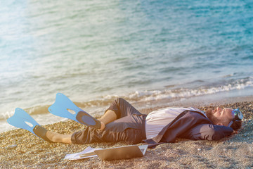 Successful businessman wearing snorkeling tools is working on the beach with laptop.