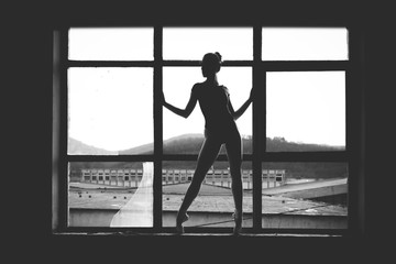 Fototapeta na wymiar Black and white photo of ballerina in the window frame in an old building.