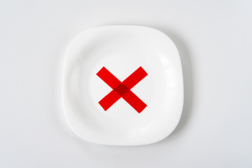 white plate with with red X cross mark on it on white table. Diet concept.
