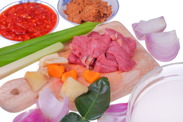 Food preparation detail - fresh red beaf meat on cutting board  with coconut milk , onion, garlic, lemon grass, ginger , turmeric, kerisik, chili and leaf turmeric