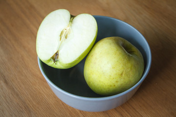 Large yellow apple and half an apple in a gray bowl on a wooden surface, selective focus