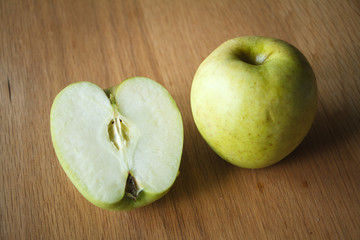Large yellow apple and half an apple on a wooden surface, selective focus
