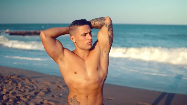 Tattooed bodybuilder sexy male coach at the beach. He walks and shows his muscles