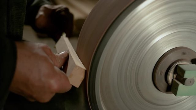 SLOW MOTION, CLOSE UP: Unrecognizable man sandpapering a piece of wood into a knife handle in his home workshop. Sawdust flying off block of wood being made into a handle by the experienced craftsman.