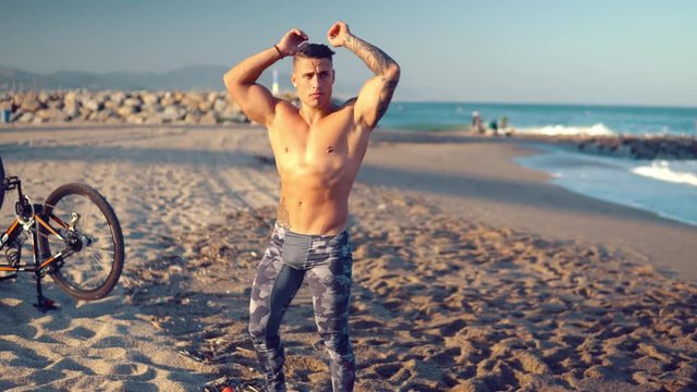 Tattooed bodybuilder sexy male coach at the beach. He walks and shows his muscles