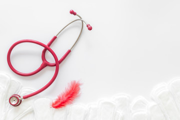 Gynaecologist and woman health concept with stethoscope, feather and sanitary pads on white background top view mock up