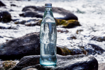 A bottle of fresh, cool water against the backdrop of nature, a mountain river with the purest water.