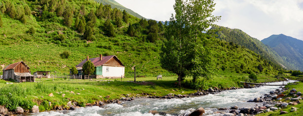 Old decrepit farmhouse surrounded by mountains and a mountain river with a blue sky. It is located in the mountains of Tien Shan.