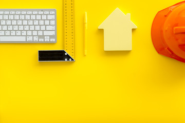 Constructor office desk with tools, helmet, ruler, keyboard and house figure on yellow background top view mock-up