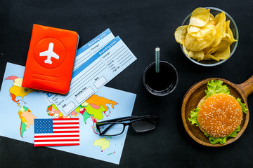 travel for traditional usa cuisine with burgers, drink, chips, passport, tickets, flag and map black background top view