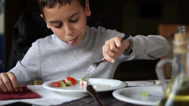 Boy eating fresh green salad in an outdoor cafee. Healthy lifestyle