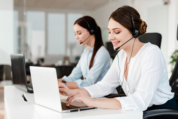 Smiling young office worker with a headset  answering in a call center, woman talking with clients....