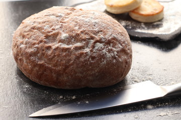 Fresh handmade bread on a dark wooden background, next to cheesecakes on a tray and a metal knife