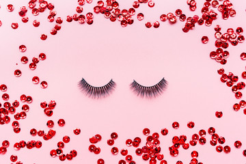 False eyelashes black color and red confetti lying on pink background. Beauty and makeup concept. Flatlay, mockup, overhead, top view copy space