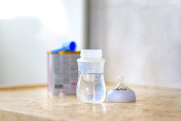 Preparation of mixture baby feeding on marble background in morning kitchen. Feeding bottle with water and baby milk formula with spoon on table.Selective focus.
