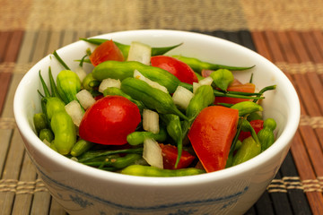 Close up bowl of steamed radish seed pods with cherry tomatoes and diced onions.