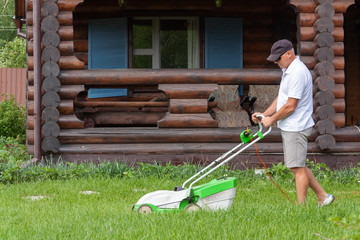 A man mows the grass with a lawn mower in the backyard