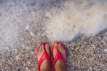 Male legs in red slaps on the shore with shells and foam