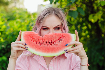 Beautiful young woman with pink hair holding juicy watermelon close to the face