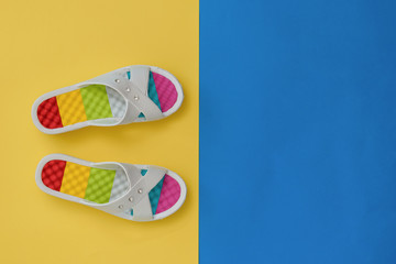 White flip-flops with colourful soles in yellow and blue background. The concept of a holiday by the sea. Flat lay.