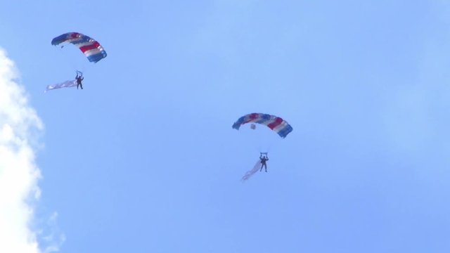 Two people flying with parachutes at an air show in Berlin. The weather is sunny with a few clouds.