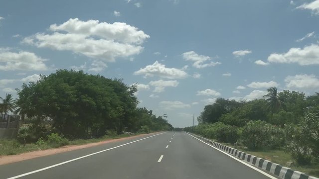 a beautiful view of empty highway with trees and bushes on both side of the roads and a beautiful sky over head