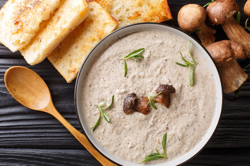 Puree soup with fresh porcini mushrooms and thyme close-up in a bowl served with toast. horizontal top view