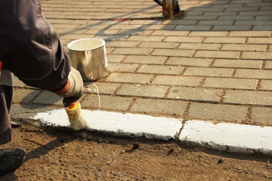 man round brush paints white paint curbstone near the road, close-up