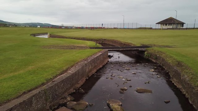 Scottish seaside links golf course with a small river winding through and bridge crossing