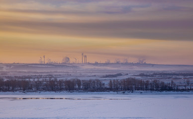 Fototapeta premium Panoramic view on frozen river and forest on hill in winter during sunset from hill