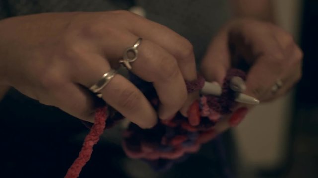 A closeup to a woman's hands doing Pink and purple wool crafts knitting with stitches.