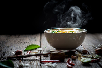 Noodles with steam and smoke in bowl on wooden background, selective focus. Asian meal on a table,...