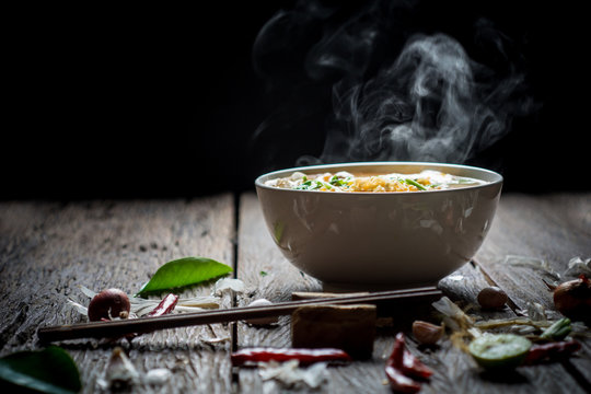 Noodles with steam and smoke in bowl on wooden background, selective focus. Asian meal on a table, junk food concept