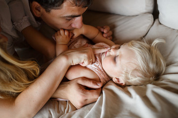 young parents hugging smiling one year old girl lying on the sofa at home