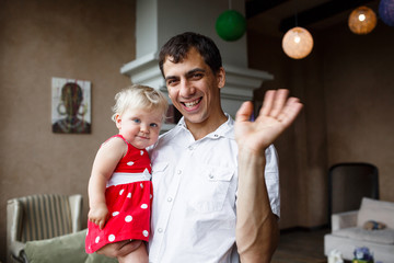 Portrait of happy father waving his hand and 1 years old daughter at home
