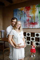 Family portrait. Happy couple holding a little girl. Awesome mom is pregnant