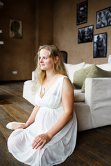 Portrait of a beautiful long-haired pregnant blonde, gracefully sitting on floor