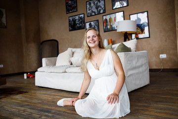Portrait of a beautiful long-haired pregnant blonde, gracefully sitting on floor