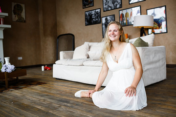 Portrait of a beautiful long-haired pregnant blonde, gracefully sitting on floor