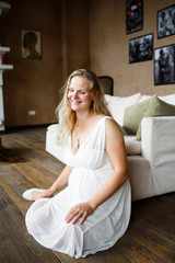 Portrait of a beautiful long-haired pregnant blonde, gracefully sitting on floor