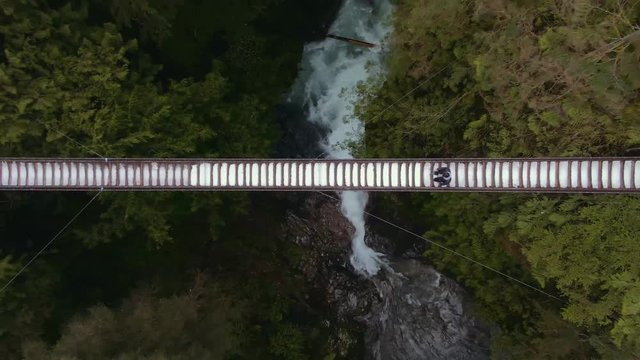 Drone shot : Drone flying up on Man walking on suspension bridge, drone shot of man on suspension bridge. Capilano and Lynn valley canyon.