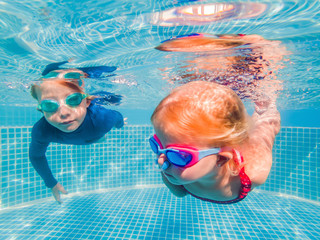 Naklejka premium Kids having fun playing underwater in swimming pool on summer vacation