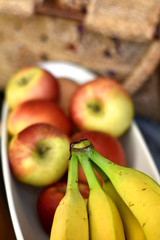 Fruit bowl with bananas and apples. Green bananas peduncle in selective focus, on the blurred background of red apples and brown rustic bag. Vertical composition, shallow dof, closeup.