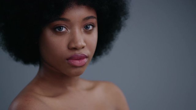Portrait of wonderful nude black young woman with afro hairstyle looking straight against grey background. Pretty african girl posing on camera.