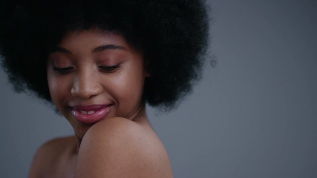 Close-up portrait of elegant pretty african girl smiling and flirting on camera. Attractive black girl with naked shoulders isolated on dark background.