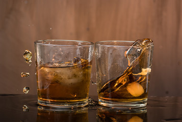 Two glasses of whiskey with ice hit and break, pouring a lot of spray and drops