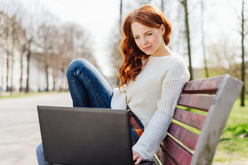 frau sitzt auf einer bank im park und schaut auf ihren laptop